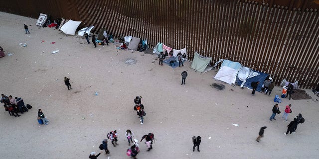 In an aerial view, Immigrants gather along the U.S. border wall after crossing through a gap in the structure from Mexico in Yuma, Arizona, on Dec. 10, 2021.