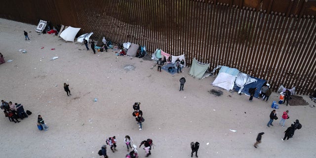 In an aerial view, Immigrants gather along the U.S. border wall after crossing through a gap in the structure from Mexico in Yuma, Arizona, on Dec. 10, 2021.