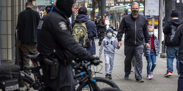 A family walks past Seattle police on 3rd Avenue on March 11, 2022, in Seattle, Washington. Police set up a mobile precinct to curb the heavy crime and drug use there, only a block away from Seattle's iconic Pike Place Market. 