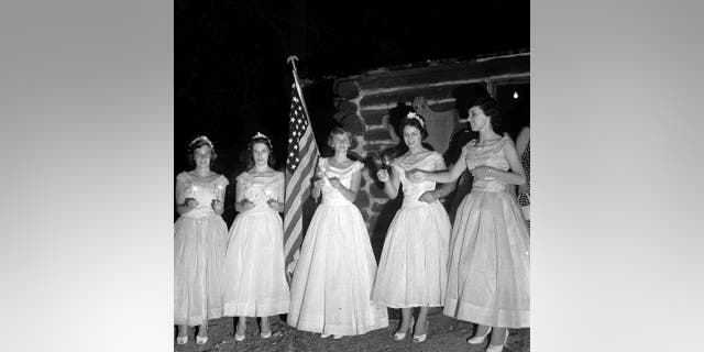 Pageant contestants stand on a stage and light sparklers during The Queen of Candles, circa 1955.