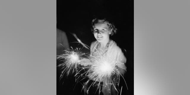 A girl holds two sparklers during a July 4th celebration, circa 1930.