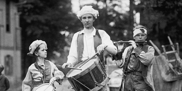 A boy plays a flute while two other boys play the drums on July 4th, circa 1922.