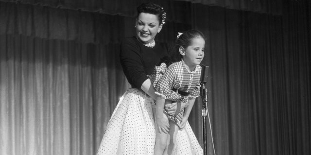 During a performance, Judy Garland holds her daughter Lorna Luft up to the microphone.