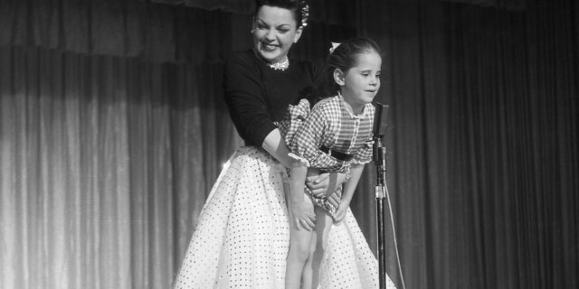 During a performance, Judy Garland holds her daughter Lorna Luft up to the microphone.