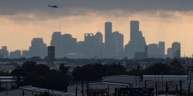 A helicopter hovers above the Houston skyline as sunlight breaks through storm clouds 