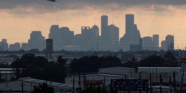 A helicopter hovers above the Houston skyline as sunlight breaks through storm clouds