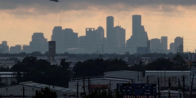 A helicopter hovers above the Houston skyline as sunlight breaks through storm clouds 