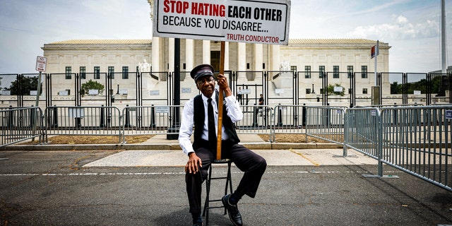 A man holds a sign outside the Supreme Court telling protesters not to hate each other.