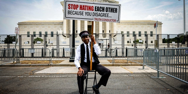 A man holds a sign outside the Supreme Court telling protesters not to hate each other.