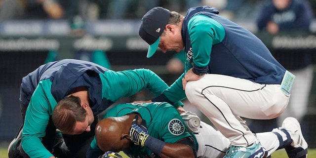 Seattle Mariners' Justin Upton, center, points to where he was hit by a pitch during the fifth inning of a baseball game against the Los Angeles Angels as he is examined by a trainer, left, and manager Scott Servais, right, Friday, June 17, 2022, in Seattle. Upton left the game after the injury. 