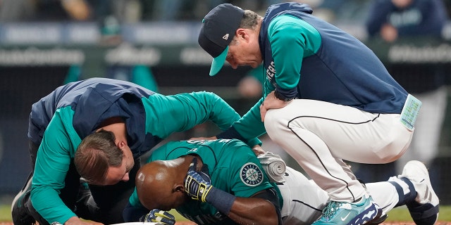 Seattle Mariners' Justin Upton, center, points to where he was hit by a pitch during the fifth inning of a baseball game against the Los Angeles Angels as he is examined by a trainer, left, and manager Scott Servais, right, Friday, June 17, 2022, in Seattle. Upton left the game after the injury.