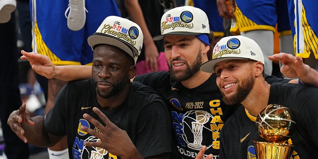 Draymond Green #23, Klay Thompson #11 and Stephen Curry #30 of the Golden State Warriors smile and celebrates on stage with he Bill Russell Finals MVP Trophy after winning Game Six of the 2022 NBA Finals against the Boston Celtics on June 16, 2022 at TD Garden in Boston, Massachusetts.
