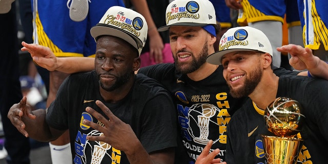 Draymond Green #23, Klay Thompson #11 and Stephen Curry #30 of the Golden State Warriors smile and celebrates on stage with he Bill Russell Finals MVP Trophy after winning Game Six of the 2022 NBA Finals against the Boston Celtics on June 16, 2022 at TD Garden in Boston, Massachusetts.