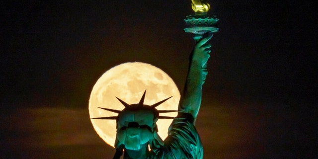 The Strawberry Supermoon rises in front of the Statue of Liberty in New York, late Tuesday, June 14, 2022. 