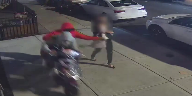 The individual riding on the back of the moped is seen grabbing the victim's purse.