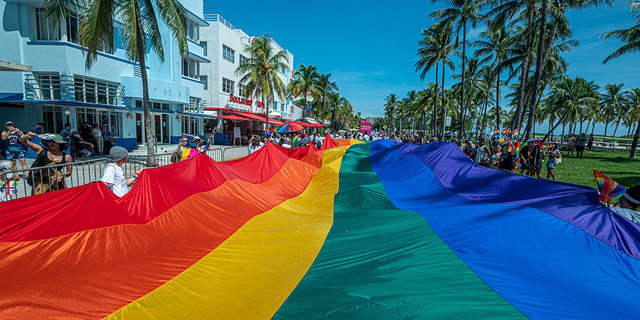 A huge multi-colored flag flies over Ocean Drive as people participate in the Pride Parade, during the Miami Beach Pride Festival, in Lummus Park, South Beach, Florida on September 19, 2021.