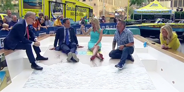 "Fox and Friends" co-hosts and home improvement expert Skip Bedell dip their toes in the water, so to speak, of San Juan Pool's Baja Beach 3D-printed fiberglass pool model at Fox Square, on June 29, 2022. (Fox News)