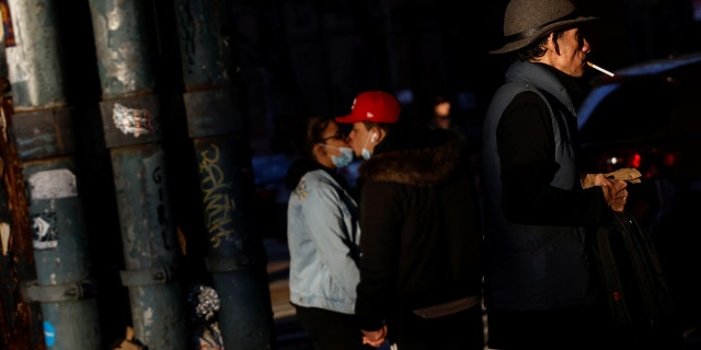 A man walks along a street corner smoking a cigarette while a couple kisses in the Brooklyn borough of New York City, U.S., February 10, 2022.