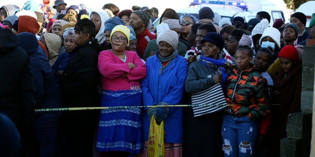 People are standing behind a police cordon outside a nightclub in East London, South Africa, on Sunday, June 26, 2022. South African police are investigating at least 20 deaths early Sunday morning at a nightclub in a coastal town in East London. It is unknown what led to the deaths of the young people who allegedly attended a party celebrating the end of the winter school exams.  (AP photo)