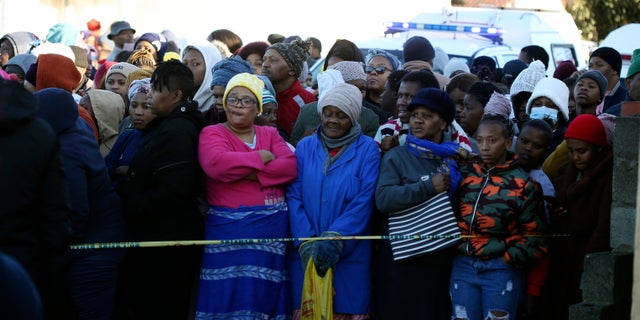 People are standing behind a police cordon outside a nightclub in East London, South Africa, on Sunday, June 26, 2022. South African police are investigating at least 20 deaths early Sunday morning at a nightclub in a coastal town in East London. It is unknown what led to the deaths of the young people who allegedly attended a party celebrating the end of the winter school exams.  (AP photo)