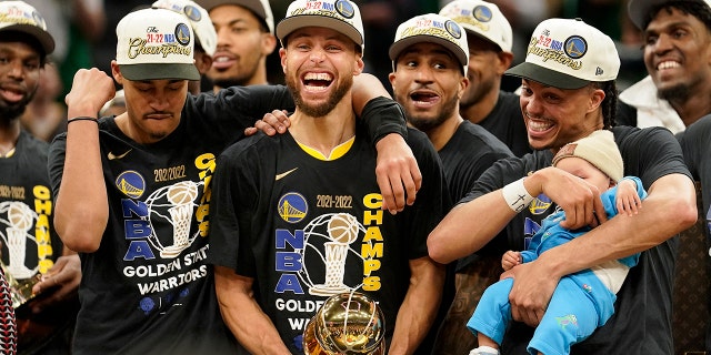 Golden State Warriors guard Stephen Curry, center, celebrates with teammates as he holds the Bill Russell Trophy as MVP after the Warriors beat the Boston Celtics in Game 6 to win an NBA title Thursday, June 16, 2022, in Boston.