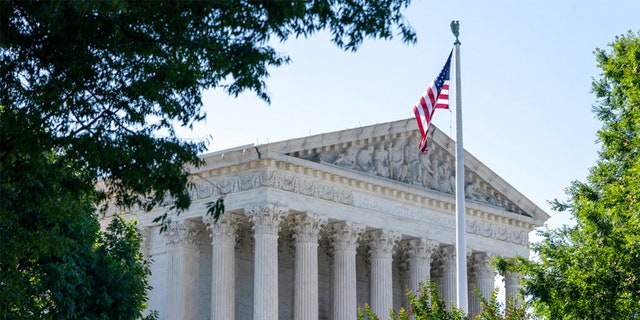 US Supreme Court building framed by trees, US flag in front