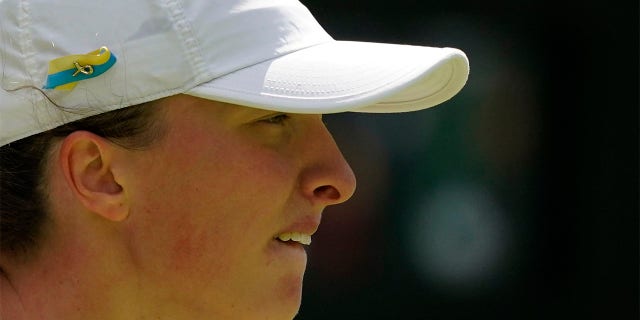 Poland's Iga Swiatek sporting a Ukrainian colors ribbon on her hat waits to receive serve from Croatia's Jana Fett in a first round women's singles match on day two of the Wimbledon tennis championships in London, Tuesday, June 28, 2022.