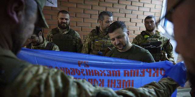 Ukrainian President Volodymyr Zelenskyy, center, looks at a flag of a military unit close to front line in Donetsk region, Ukraine, Sunday, June 5.