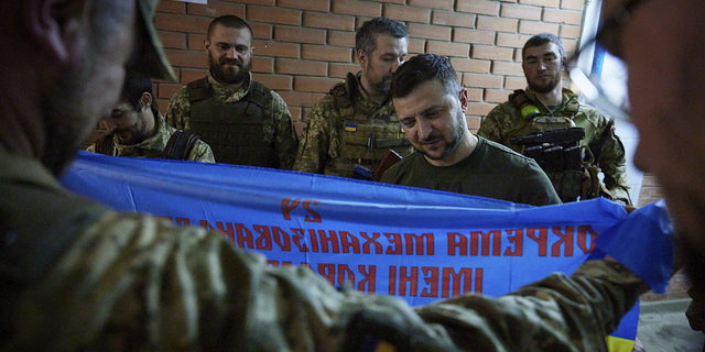 Ukrainian President Volodymyr Zelenskyy, center, looks at a flag of a military unit close to front line in Donetsk region, Ukraine, Sunday, June 5.