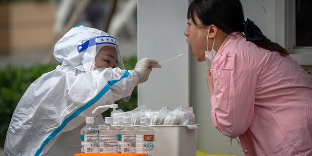 A worker wearing a protective suit swabs a woman's throat for a COVID-19 test at a coronavirus testing site in Beijing, Thursday, June 9, 2022.