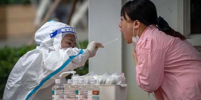 A worker wearing a protective suit swabs a woman's throat for a COVID-19 test at a coronavirus testing site in Beijing, Thursday, June 9, 2022.