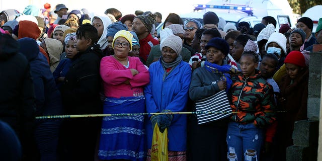 People stand behind a police cordon outside a nightclub in East London, South Africa, Sunday June 26, 2022. 