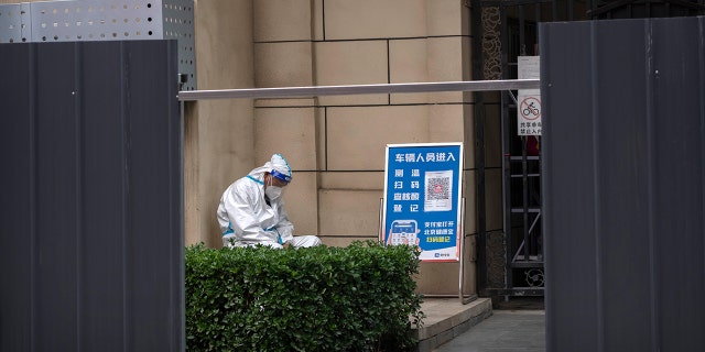 On Tuesday, June 14, 2022, as part of COVID-19 control in Beijing, a man in a protective suit sits at the entrance to a house surrounded by metal barricades.