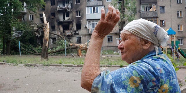 2022 年 6 月 22 日，星期三，在乌克兰东部顿涅茨克人民共和国政府管辖的顿涅茨克，一名妇女在炮击中受损的一栋公寓楼附近做手势。