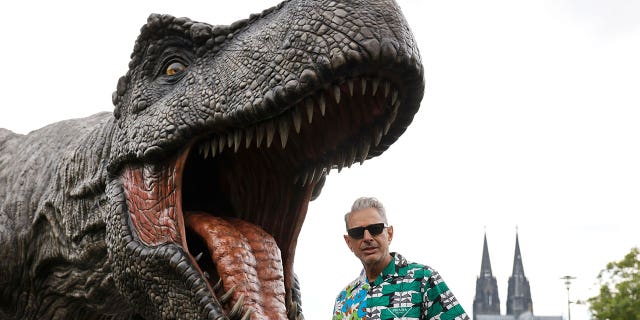 Jeff Goldblum stands in front of a T-Rex figure, with the Cologne Cathedral in the background, during a photocall for "Jurassic World: Dominion," in Cologne, Germany, May 29, 2022.