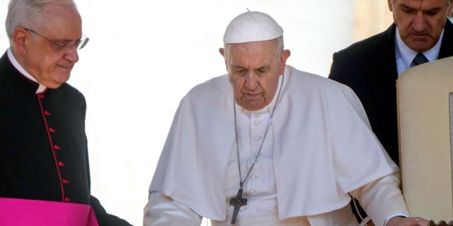 Pope Francis is helped by his aide Monsignor Leonardo Sapienza, left, as he walks with a cane to his weekly general audience in St. Peter's Square at the Vatican on June 1, 2022.