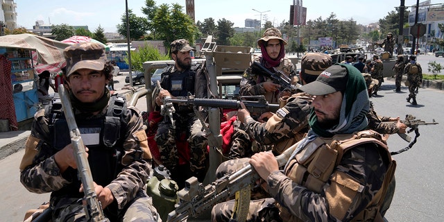 Taliban fighters guard explosion site dressed in miitary uniforms and holding weapons