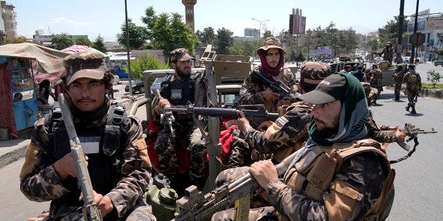 Taliban fighters guard explosion site dressed in miitary uniforms and holding weapons