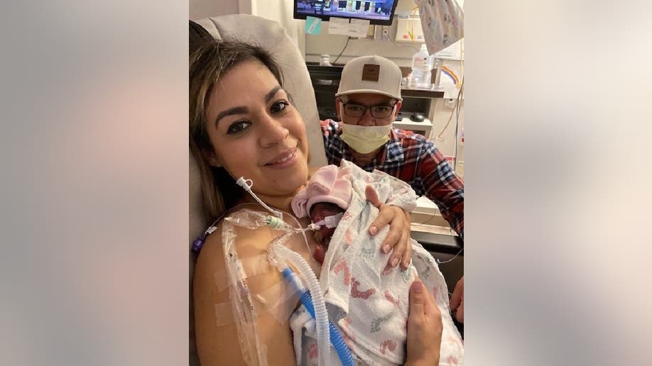 Carmen holds one of her twin girls from her hospital bed while her boyfriend Johnny looks on.