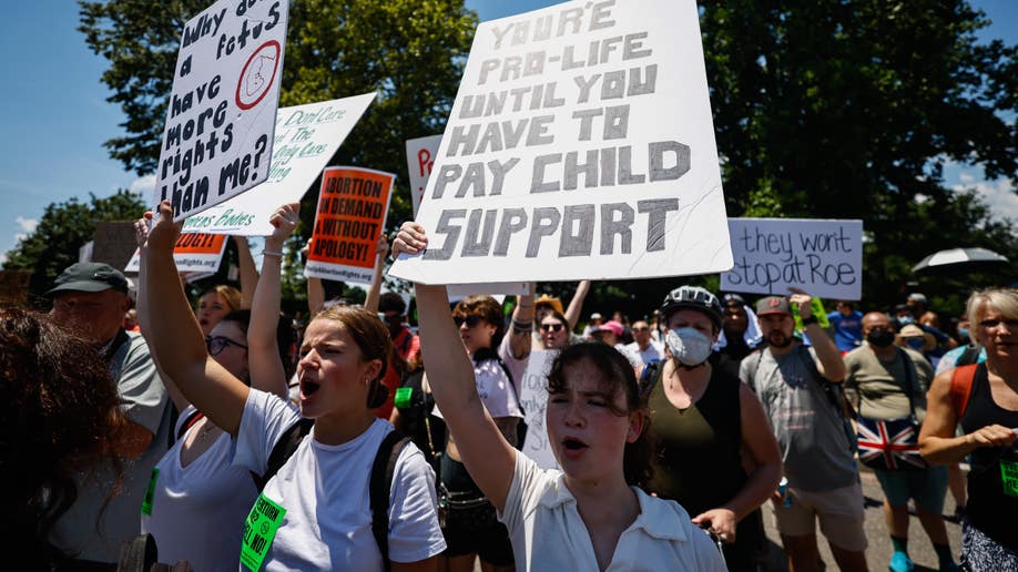 A woman holds a 'You're pro-life until you have to pay child support' sign.