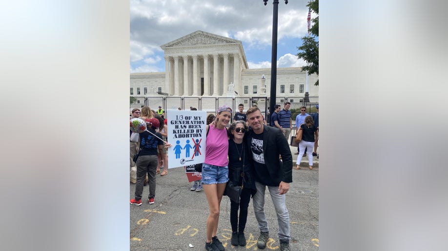 Three people pose in front of the Supreme Court
