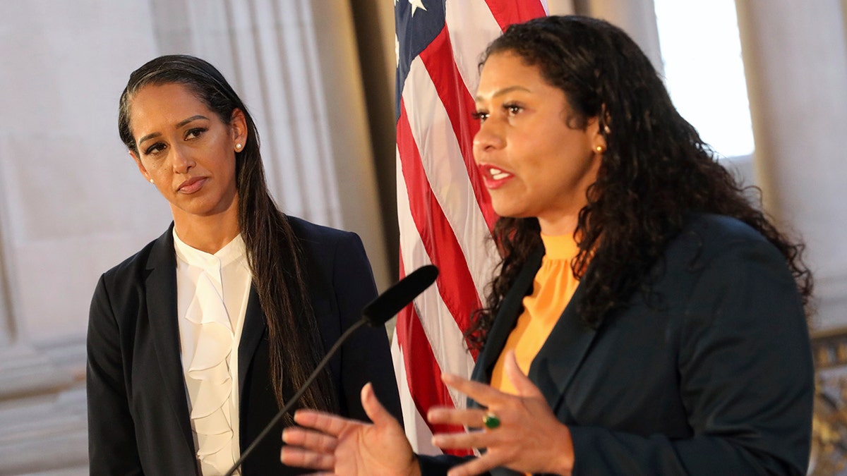 San Francisco Mayor London Breed in an orange top speaks as Brooke Jenkins looks on in a black and white suit