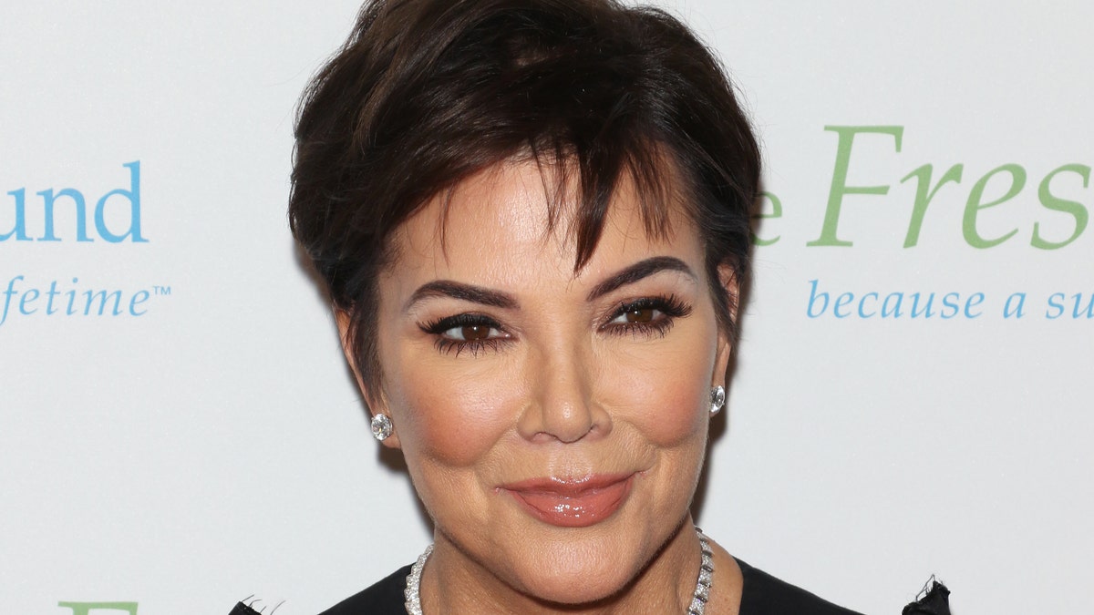 Kris Jenner smiles on the red carpet wearing a black dress and diamond necklace