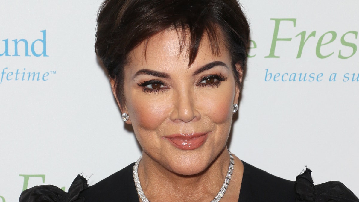 Kris Jenner smiles on the red carpet wearing a black dress and diamond necklace