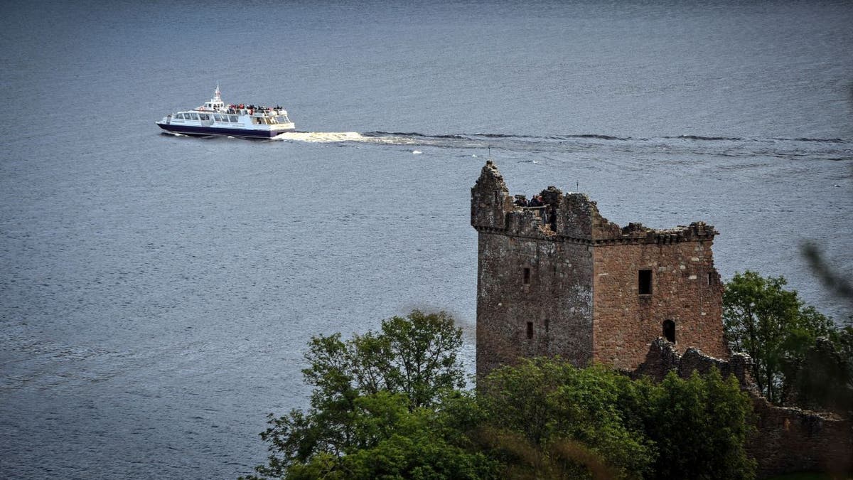A boat floats on Loch Ness in Scotland, with a castle in the foreground