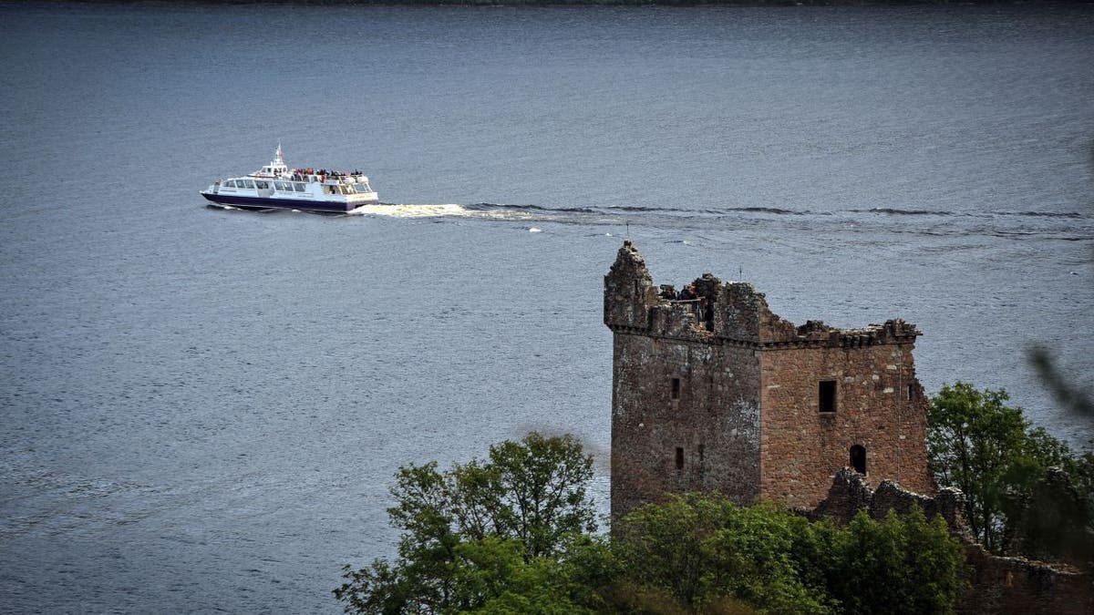 A boat floats on Loch Ness in Scotland, with a castle in the foreground