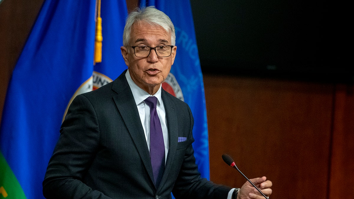 Los Angeles DA George Gascon wearing glasses in a black suit speaking in front of a microphone