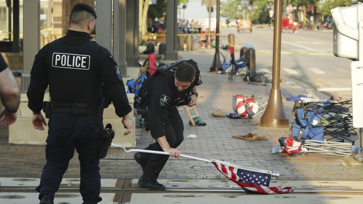 A police officer picks up a water-logged American flag, Tuesday, July 5, 2022, left behind after Monday&apos;s mass shooting in Highland Park, Illinois.