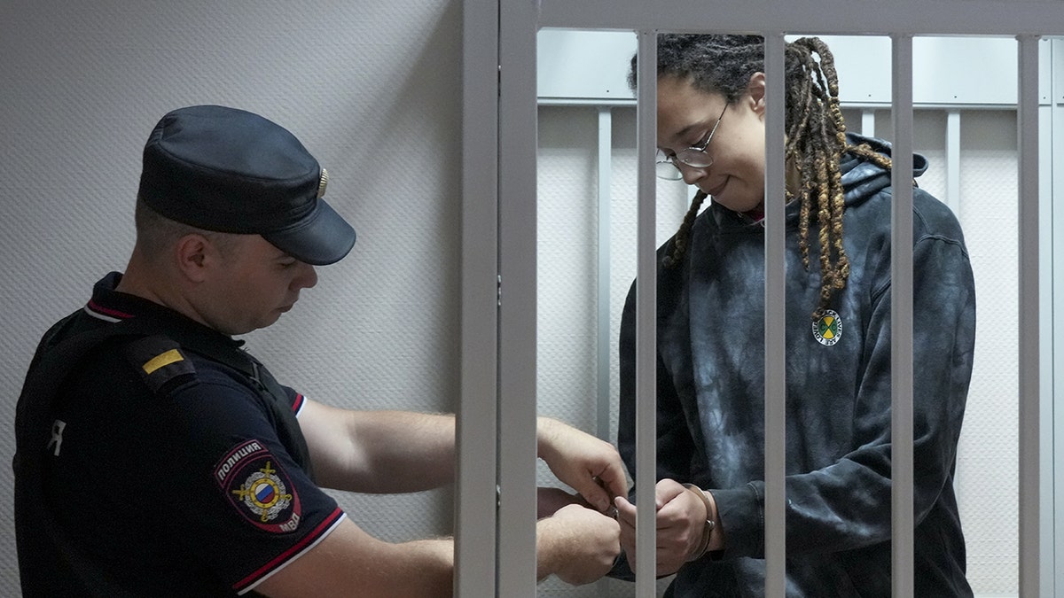 A photo of Brittney Griner in a cell as a guard stands outside