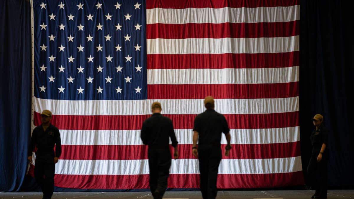Navy soldiers walk in front of an American Flag